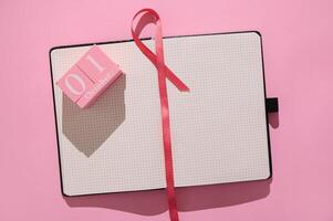 Open notebook with pink ribbon and October 1st calendar block on pink background photo
