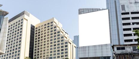 A large blank billboard hangs on the side of a tall building in a city. The billboard is white and has a blue sky in the background. photo