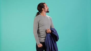 Man holding jacket in one hand while looking around, contemplating, creating a sense of curiosity. Person holding coat showing curiosity for surroundings, studio background, camera A video