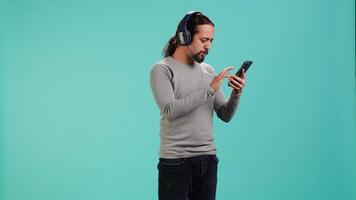 Relaxed man having fun listening to music from mobile phone, studio backdrop. Carefree person hearing tunes playing from smartphone device, isolated over studio background. camera A video