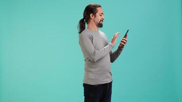 Man scrolling on smartphone touchscreen, using mobile phone to check social media feed, studio backdrop. Person browsing internet websites, isolated over studio background, camera A video