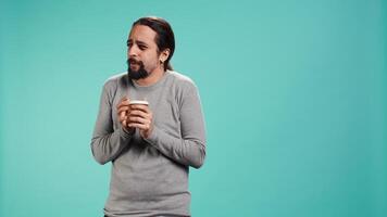 Man closes eyes while tasting and enjoying delicious coffee, isolated over blue studio backdrop. Person drinks caffeinated beverage to gain energy and be able to do doing productivity tasks, camera B video
