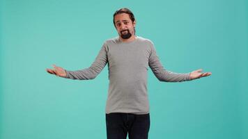 Man shrugging shoulders, expressing uncertainty or helplessness, having troubled facial expression. Person unable to provide assistance to friend, feeling powerless, studio background, camera A video