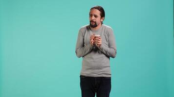 Man closes eyes while tasting and enjoying delicious coffee, isolated over blue studio backdrop. Person drinks caffeinated beverage to gain energy and be able to do doing productivity tasks, camera A video