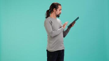 man bläddring fastän finansiell granska Rapportera på läsplatta, isolerat över blå studio bakgrund. arbetstagare läsning pappersarbete på digital bärbar enhet, lösning företag uppgifter, kamera en video