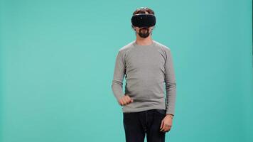 Tech enthusiast wearing virtual reality goggles, doing zooming in gestures. Arab man using high tech futuristic modern VR glasses, making tactile touching gesturing, studio background, camera A video