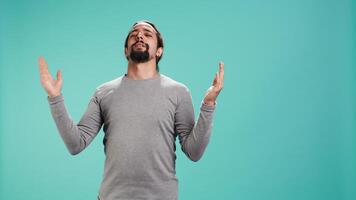 Cheerful pious man looking up to sky, waiting for sign from his god. Happy spiritual man doing worship hand gesturing, waiting for miracle, isolated over studio background, camera B video