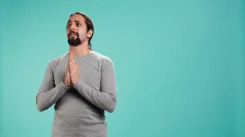Portrait of man putting hands together in begging gesture, making wish, hoping for good news isolated over studio background. Person waiting for results, praying for positive outcome, camera B video