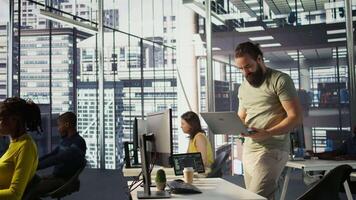 Admin at office desk utilizing cloud computing resources on laptop to train large scale machine learning models. Man monitoring company systems using notebook while standing in workspace, camera B video