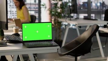 Green screen laptop on desk in workspace with admins in background doing software quality assurance. Chroma key notebook in office with woman at work inspecting coding on device, camera A video