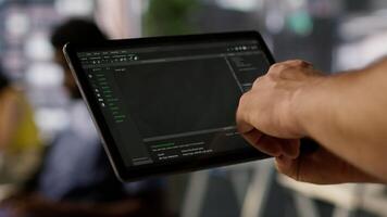 Data scientist uses tablet to check on machine learning models that can analyze data to automate decision making processes. Close up of IT specialist using device to do programming in office, camera A video