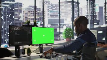 Developer with disability sitting in wheelchair fixing applications issues on green screen PC. Man with paraplegia optimizing company software with mockup computer, camera B video
