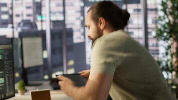Programmer developing machine learning APIs solving complex problems, checking performance on tablet. Man training predictive models capable of handling resource intensive tasks, camera A video