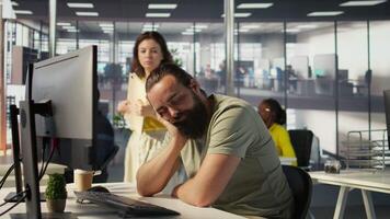 Tired company worker caught falling asleep at desk in office by colleague, laughing about it. Exhausted man sleeping in front of computer screen in workplace, woken up by amused coworker, camera B video