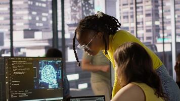 Admin assisted by coworker while utilizing cloud computing resources to train large scale machine learning models. Woman and colleague monitoring AI company systems using computer, camera A video