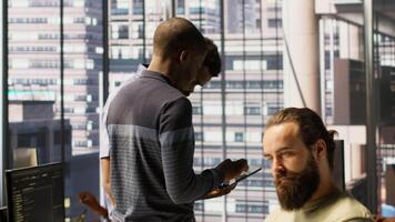 Technician and colleague using device for managing cloud computing platforms training machine learning models. IT staff members in office monitoring company systems using tablet, camera A video