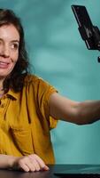 Vertical Influencer in home studio using smartphone on selfie stick to record live broadcast, greeting subscribers. Online star hosts q and a session with viewers using mobile phone, camera A video