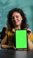 Vertical Jolly woman filming tech tutorial on how to repair damaged mockup tablet. Joyous tech professional in home studio teaching subscribers to install operating system on isolated screen device, camera B video