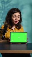 Vertical Upbeat technology specialist at home holding newly launched green screen tablet in hand, presenting specs. Joyous internet star doing mockup portable digital device review for viewers, camera B video