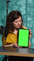 Vertical Woman holding green screen tablet, talking about specifications, filming with professional camera. Internet show host presenting chroma key device features, recording with filming gear, camera A video