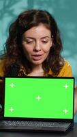 Vertical Influencer in home studio using recording tech to capture live broadcast, reviewing chroma key laptop. Online show host filming electronics haul, presenting green screen notebook for viewers, camera A video
