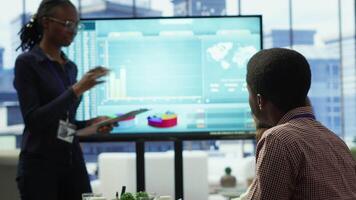 Diverse group of professionals meeting to discuss a new development strategy, utilizing infographics and monthly analysis numbers to reach target and accomplish organizational goals. Camera A. video
