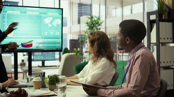 Diverse group of professionals meeting to discuss a new development strategy, utilizing infographics and monthly analysis numbers to reach target and accomplish organizational goals. Camera B. video