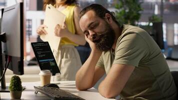 Tired company worker caught falling asleep at desk in office by colleague, laughing about it. Exhausted man sleeping in front of computer screen in workplace, woken up by amused coworker, camera A video
