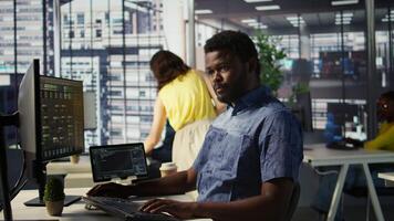 Man checking paperwork details on computer screen, solving tasks. African american bookkeeper in office making sure documents are compliant with quality assurance expectations and standards, camera B video