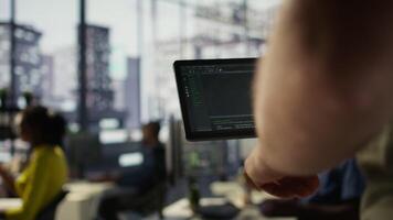 Data scientist uses tablet to check on machine learning models that can analyze data to automate decision making processes. Close up of IT specialist using device to do programming in office, camera B video