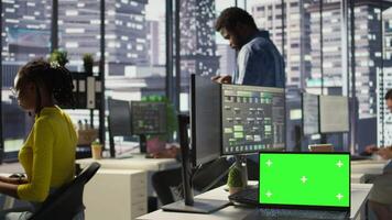 Green screen laptop on desk in workspace with admins in background doing software quality assurance. Chroma key notebook in office with woman at work inspecting coding on device, camera B video