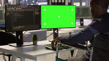 Developer with disability sitting in wheelchair fixing applications issues on green screen PC. Man with paraplegia optimizing company software with mockup computer, camera A video