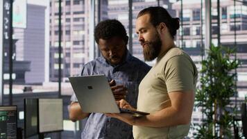 IT employees in office working together using laptop, testing and deploying programs and systems. Developer and colleague checking code on notebook, doing brainstorming in workspace, camera A video