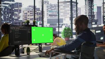 Person with disability testing and deploying programs and systems on green screen PC. Software technician in wheelchair checking code on mockup PC, sitting at desk in office, camera B video
