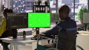 Person with disability testing and deploying programs and systems on green screen PC. Software technician in wheelchair checking code on mockup PC, sitting at desk in office, camera A video
