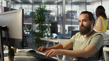 System administrator with disability in inclusive workspace training machine learning models. IT specialist with paraplegia monitoring and maintaining company systems, camera B video
