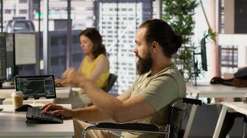 Person with impairment processing and analyzing data to automate decision making processes. IT specialist with disability programming in office, sitting in wheelchair, camera A video
