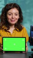 Vertical Upbeat technology specialist at home holding newly launched green screen tablet in hand, presenting specs. Joyous internet star doing mockup portable digital device review for viewers, camera A video
