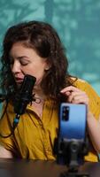 Vertical Content creator using smartphone to film ASMR for subscribers, tapping on mic. Woman in studio using professional microphone to whisper and put viewers to sleep, camera A video