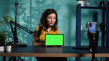 Upbeat technology specialist at home holding newly launched green screen tablet in hand, presenting specs. Joyous internet star doing mockup portable digital device review for viewers, camera B video