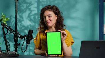 Jolly woman filming tech tutorial on how to repair damaged mockup tablet. Joyous tech professional in home studio teaching subscribers to install operating system on isolated screen device, camera A video