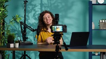 Smiling woman in studio using professional camera to record , greeting subscribers. Happy online star hosts q and a session with viewers, filming with advanced gear, camera A video