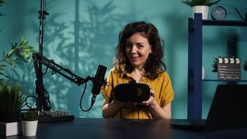 Happy tech content creator filming technology review of newly released VR glasses, unpacking them and presenting specs to fans. Jolly woman showing virtual reality headset to subscribers, camera B video