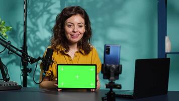 Upbeat technology specialist at home holding newly launched green screen tablet in hand, presenting specs. Joyous internet star doing mockup portable digital device review for viewers, camera A video