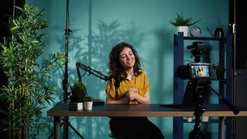 Smiling woman in studio using professional camera to record , greeting subscribers. Happy online star hosts q and a session with viewers, filming with advanced gear, camera B video