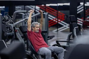 An asian senior man in sportswear doing weight lifting the machine to gain bicep and back muscle while having exercise training in the gym for longevity and retirement concept photo