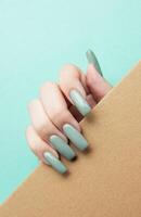 Hand holding a brown envelope with long green nails against a light blue background photo