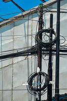 Urban chaos depicted through tangled electrical wires against a building and clear blue sky, showcasing complex city infrastructure photo