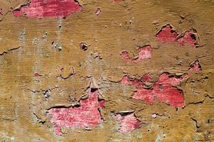 Close up of a wall with peeling red paint, revealing rough brown textures underneath. This image highlights the contrast between vibrant red and earthy brown, depicting decay and vintage appeal. photo