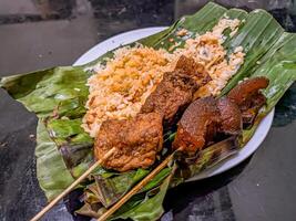 Indonesian grilled rice nasi bakar with cow nose skewers and marinated tofu skewers, served on banana leaves, showcasing traditional street food photo